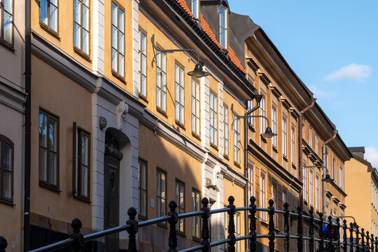 Colorful historic street presents architecture facades in Stockholm Sodermalm Sweden with metal railing strong perspective and clean daylight under blue sky