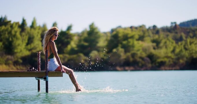 Girl enjoying a sunny day by the lake while dipping her feet in the water and surrounded by lush greenery in a scenic outdoor setting