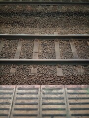 Naklejka premium Top view of railway tracks with gravel ballast and tactile paving at station platform. Transportation infrastructure and industrial background texture.
