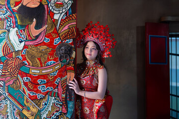 Asian woman in red traditional clothing and headdress stands by colorful door painting for Chinese New Year celebration, lunar New Year, and zodiac year of the red horse
