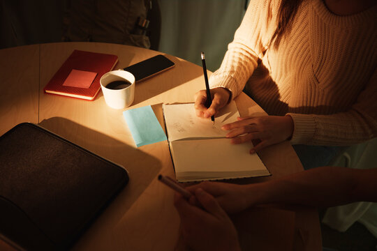 High angle view of female entrepreneur writing in diary while sitting with colleague at table in office