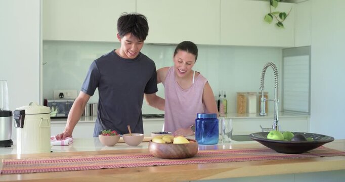 Couple greeting after man entering kitchen, arranging fruit bowl and 3 bowls at counter to serve