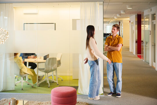 Full length of female business entrepreneur talking with male coworker while standing in office lobby