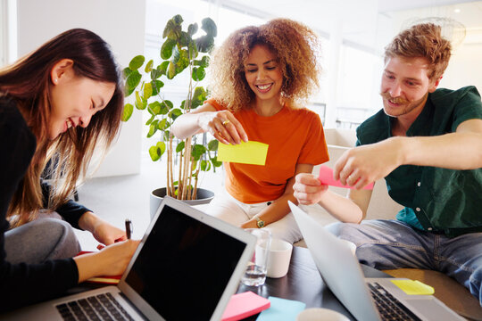 Smiling male and female business colleagues reading adhesive note while sitting in office