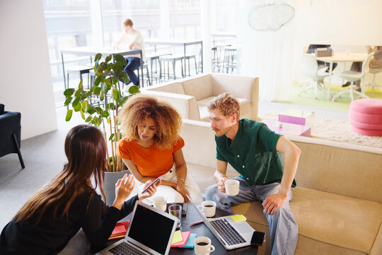 High angle view of multiracial male and female business employees looking in smart phone held by coworker at office