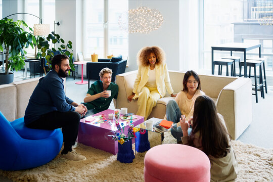 High angle view of female entrepreneur talking with group of business colleague while spending leisure time in office lobby