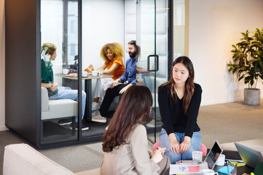 Young female business expert listening to female manager explaining ideas while sitting in coworking office