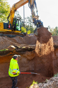 Male construction worker standing near backhoe of tractor pouring mud in hole