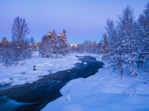 High angle view of stream flowing amidst snow covered land with trees against clear sky
