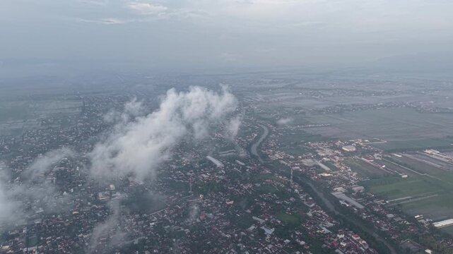 Bird&rsquo;s-eye view of a town with a winding river, surrounding farmland, and scattered neighborhoods. Clouds drift over the landscape, conveying calm, openness, and a sense of vast rural-urban mix.
