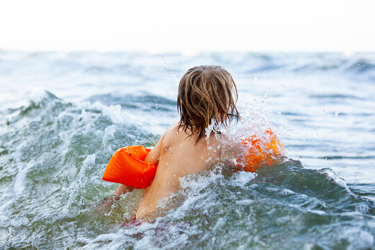 Rear view of girl swimming with water wings in wavy sea