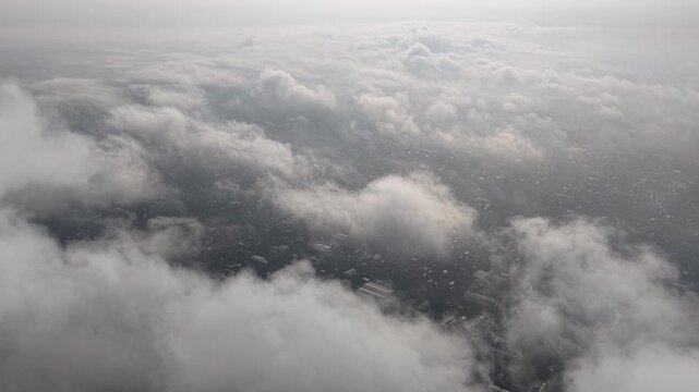 An expansive aerial scene shows a cityscape peeking through soft clouds from an airplane window, conveying travel, altitude, and the wonder of the skies.
