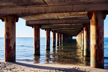 Underneath Baltic Sea pier with rusted columns and calm water