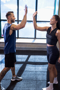 Full length of male and female athlete giving high-five while working out in gym