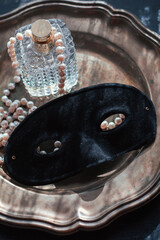 Masquerade magic: black velvet mask on shimmering mother-of-pearl tray, veiled in white feathers, crystal perfume and glowing pearls. Sultry moody light, pure mystery and bridal seduction.