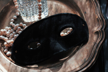 Masquerade magic: black velvet mask on shimmering mother-of-pearl tray, veiled in white feathers, crystal perfume and glowing pearls. Sultry moody light, pure mystery and bridal seduction.