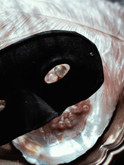 Masquerade magic: black velvet mask on shimmering mother-of-pearl tray, veiled in white feathers, crystal perfume and glowing pearls. Sultry moody light, pure mystery and bridal seduction.