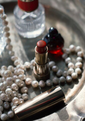 Luxury beauty flat lay: deep red perfume, gold lipstick, black case on iridescent mother-of-pearl tray with natural pearls. Soft dreamy lighting, romantic glow, feminine elegance 