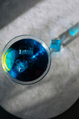 Electric blue cocktail in elegant martini glass with ice cubes and fresh lime slice. Moody dramatic lighting, sophisticated top-down view &mdash; perfect for luxury bar, party and summer refreshment concept