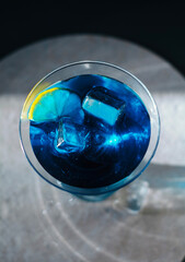 Electric blue cocktail in elegant martini glass with ice cubes and fresh lime slice. Moody dramatic lighting, sophisticated top-down view &mdash; perfect for luxury bar, party and summer refreshment concept