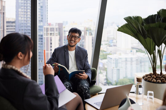 Happy businessman holding book while talking with female colleague at office