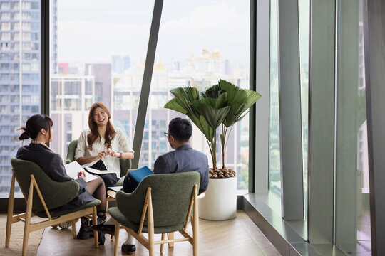 Happy businesswoman sitting with colleagues on chair during office meeting