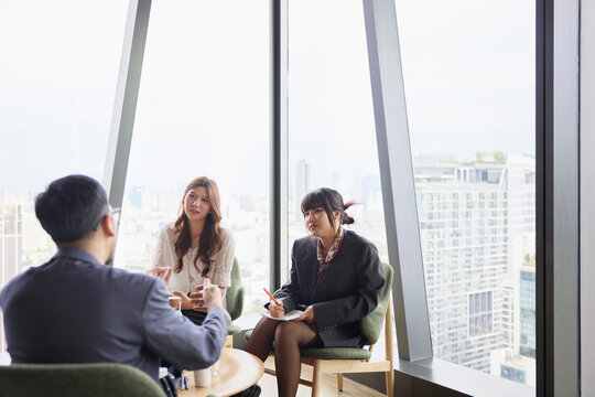 Male manager discussing strategies with female colleagues sitting on chairs at office