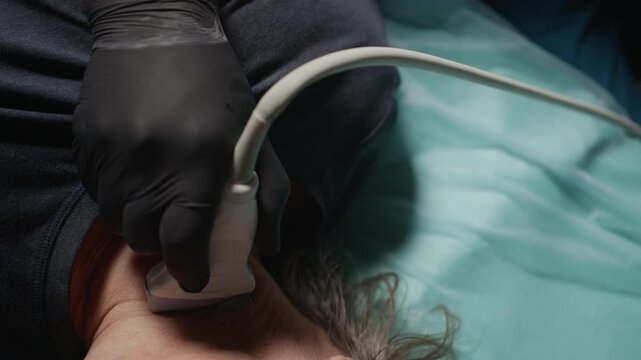 Cropped close up shot of gloved hands of unrecognizable sonographer examining thyroid of female patient, using ultrasound machine in clinic