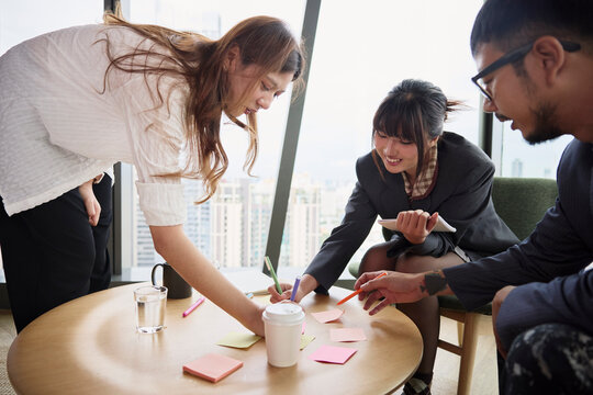 Group of male and female entrepreneurs writing on adhesive notes in meeting