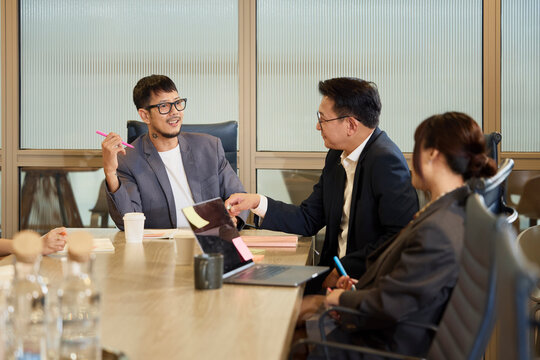 Young male colleague discussing with manager while sitting around table in meeting room