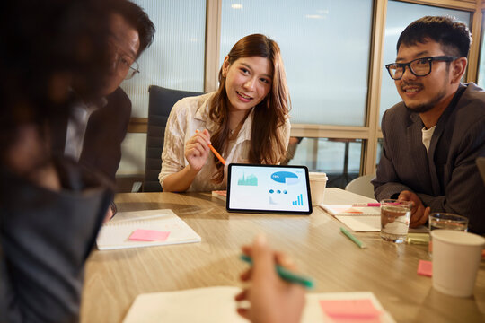 Smiling businesswoman explaining graphs over digital tablet to team at office