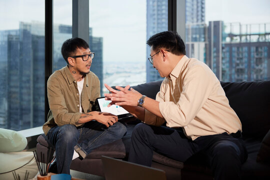 Male entrepreneur explaining business strategies to colleague sitting on sofa at office