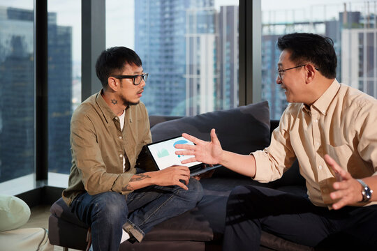 Smiling male manager discussing strategies with young colleague sitting on sofa at office
