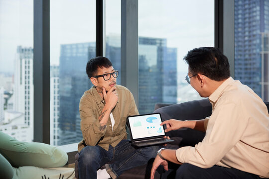 Thoughtful male entrepreneur listening to manager explaining strategies over digital tablet at office
