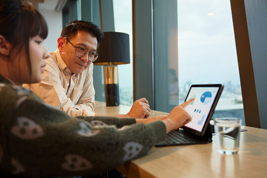 Female colleague explaining chart diagrams to manager over digital tablet at office