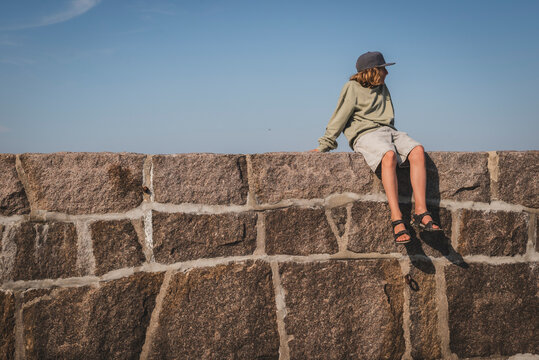 Carefree boy sitting on top of stone wall against sky