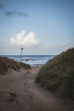 Empty dirt road leading towards beach against cloudy sky