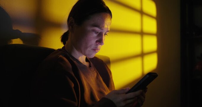 Serious Woman Using Smartphone in a Dark Room with Yellow Light