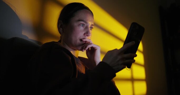 Anxious Woman Using a Smartphone at Night in a Dark Room