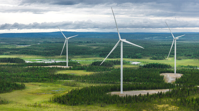 Drone point of view of wind turbines amidst trees under cloudy sky