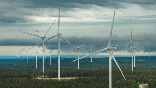 Tall wind turbines amidst trees against cloudy sky