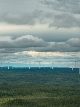 Distant view of wind turbines in row amidst trees under cloudy sky