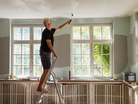 Side view of senior man painting ceiling while standing on ladder at home