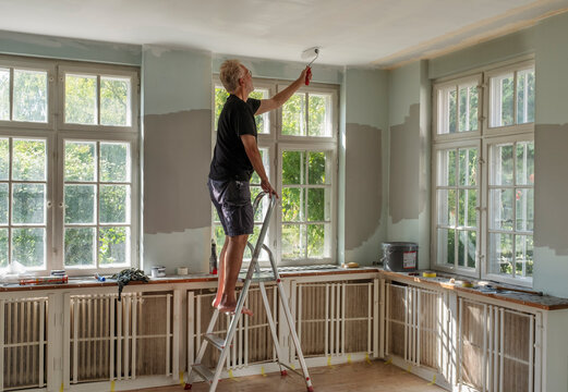 Retired man painting ceiling while standing on ladder at home