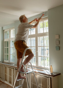 Senior man using caulk gun to apply sealant on ceiling at home