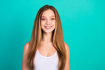 Fototapeta premium Portrait of a young woman smiling confidently against a vibrant turquoise background showcasing casual style