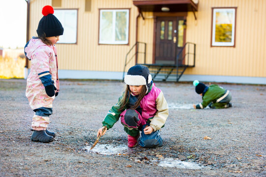 Girl looking at sister playing with stick in back yard