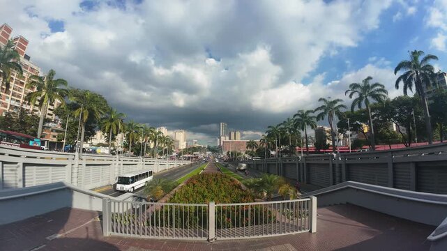 Wide-angle view of Sim&oacute;n Bol&iacute;var Avenue with palm trees, traffic, and modern city skyline during sunset. Dramatic clouds over a busy urban road