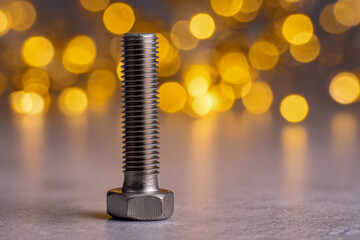 Metallic bolt standing upright on reflective surface with warm golden bokeh lights in soft-focused background creating elegant industrial contrast © Mikhail Vorobev