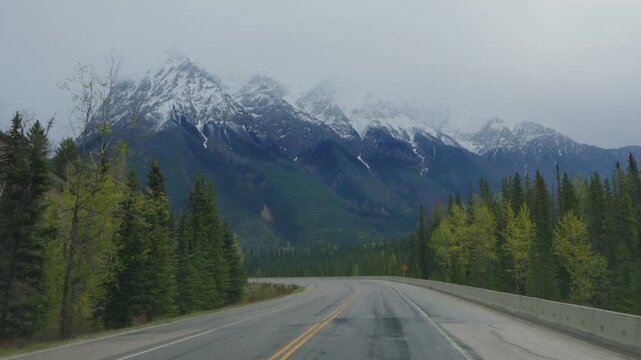 Car's perspective driving on a highway with snow capped mountains and pine trees in Yoho National Park in British Columbia, Canada